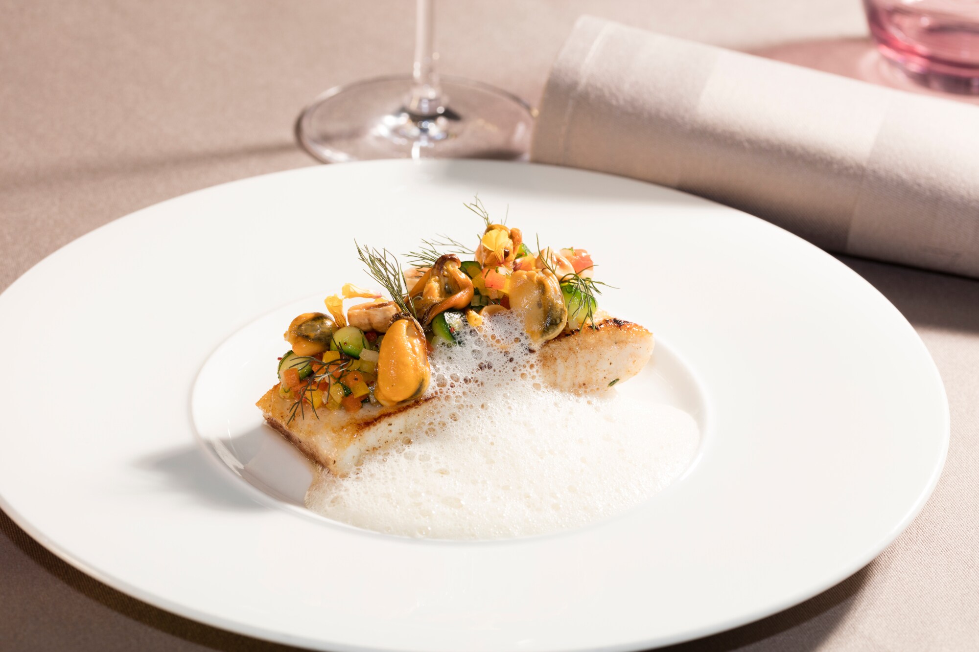 Ein Stück Fisch mit Meeresfrüchten, Dill und weißem Schaum auf einem Teller