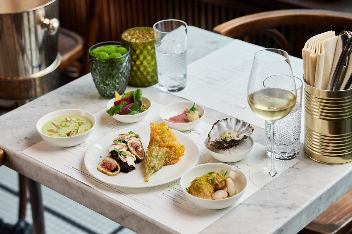 Mehrere Teller mit feinen Speisen und ein Glas Weißwein stehen auf einem Marmortisch