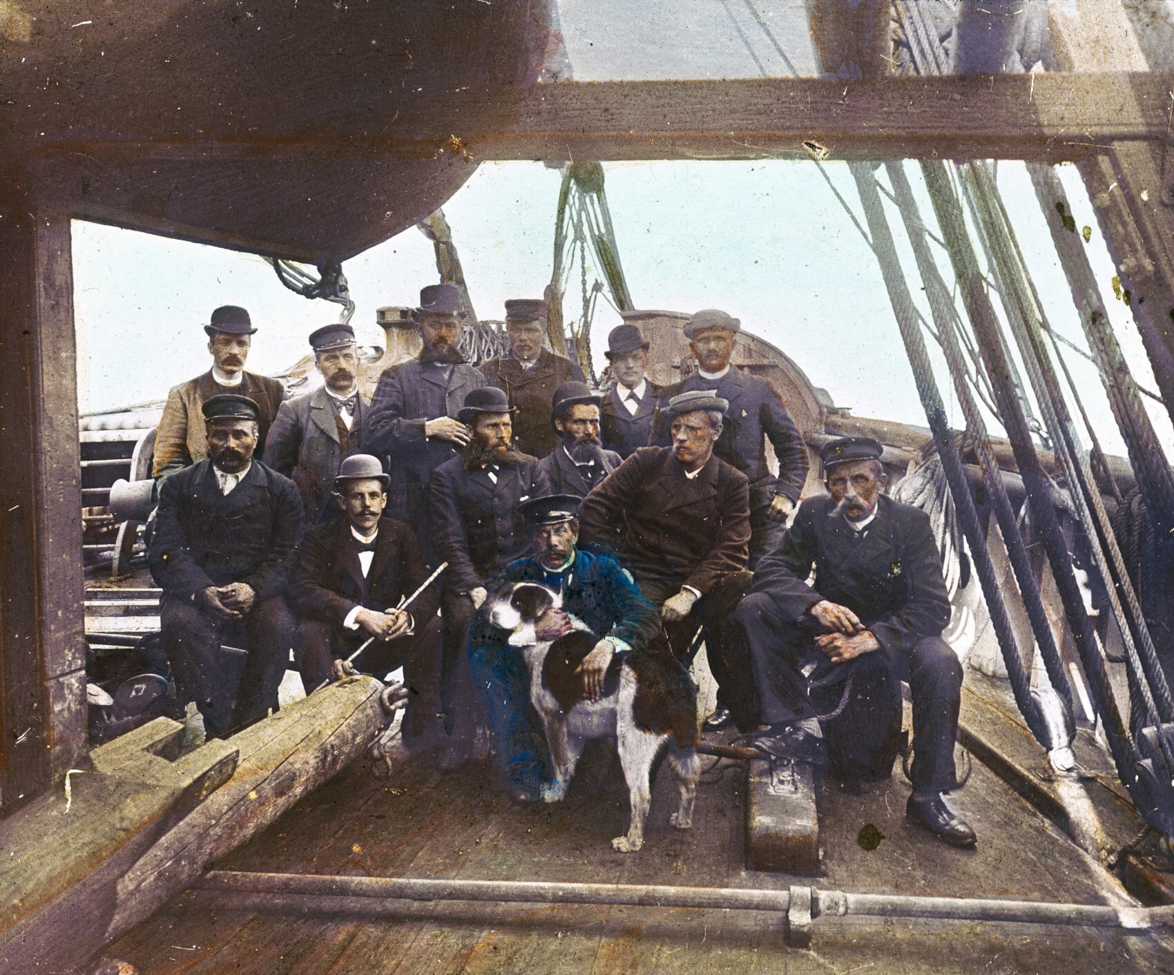 Eine Gruppe von Männern in Arbeitsanzügen und mit Hüten sowie ein Hund an Bord eines Schiffes Eine Gruppe von Männern in Arbeitsanzügen und mit Hüten sowie ein Hund an Bord eines Schiffes