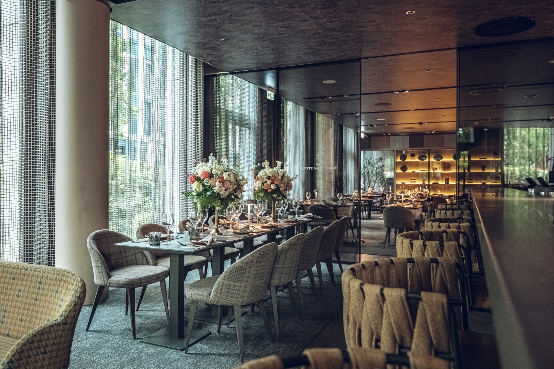 Blick ins Innere eines Restaurants mit Polsterstühlen und Blumensträußen auf den Tischen