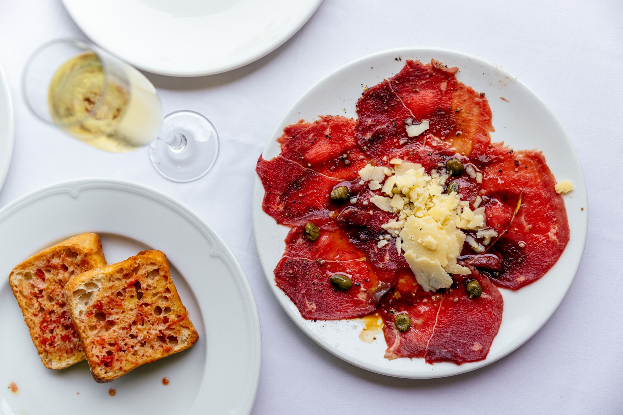 Weiße Teller mit geröstetem Brot und Carpaccio und ein Sektglas