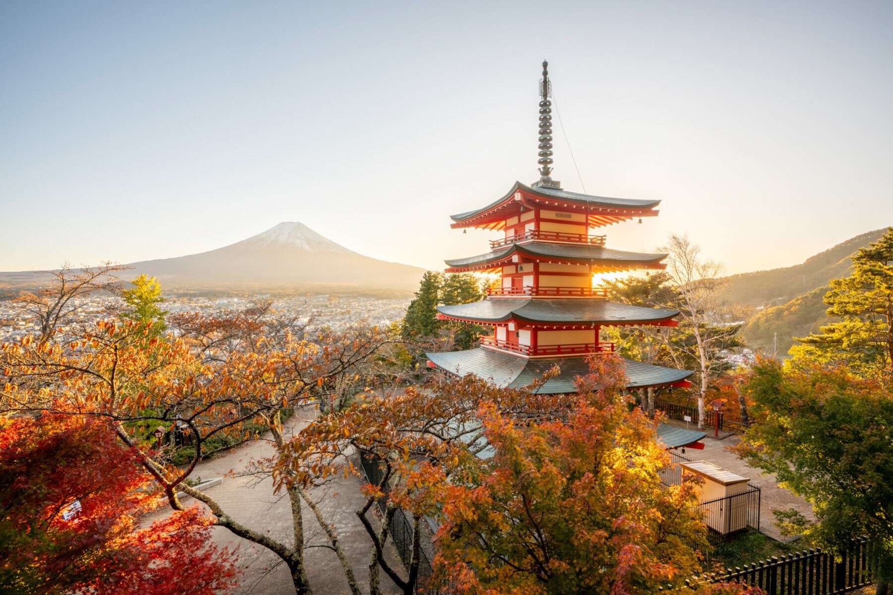 Ein mehrstöckiger, japanischer Tempel mit roten Ornamenten, im Hintergrund eine Stadt am Fuße des Mount Fuji