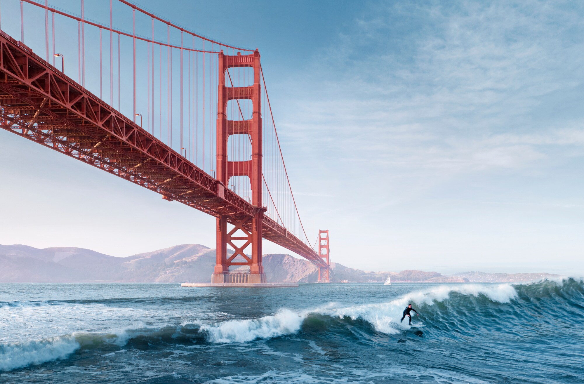 Ein Surfer auf einer Welle unter der roten Golden Gate Bridge
