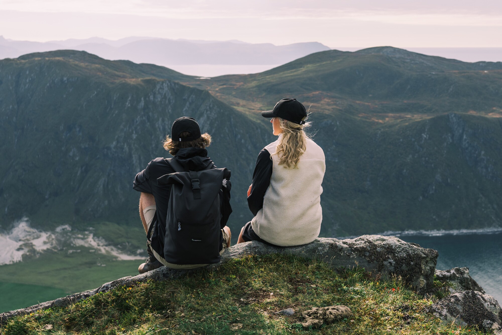 Eine Frau und ein Mann sitzen auf einem Bergvorsprung und schauen in die Ferne