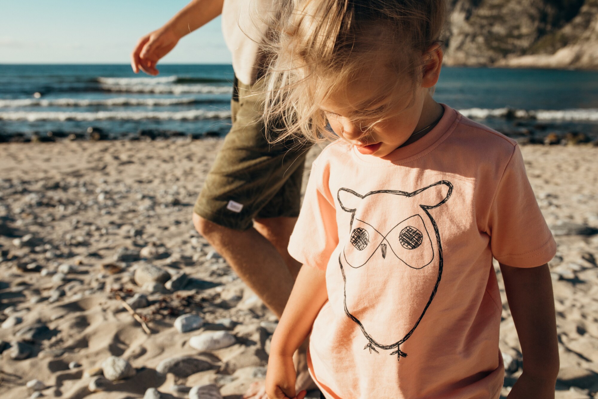 Ein kleines Mädchen am Strand trägt ein T-Shirt mit Eulen-Print