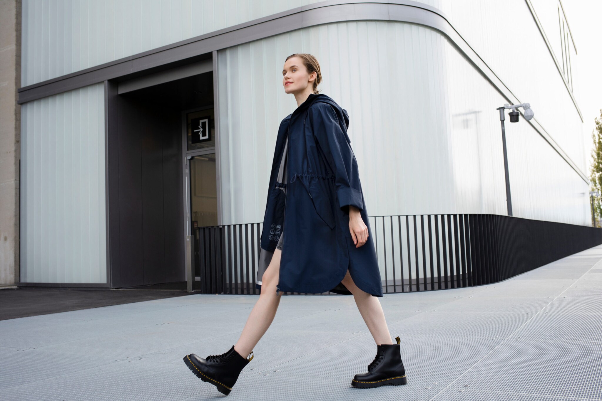 Eine Frau in einem dunkelblauen Parka läuft vor einem weißen Gebäude.