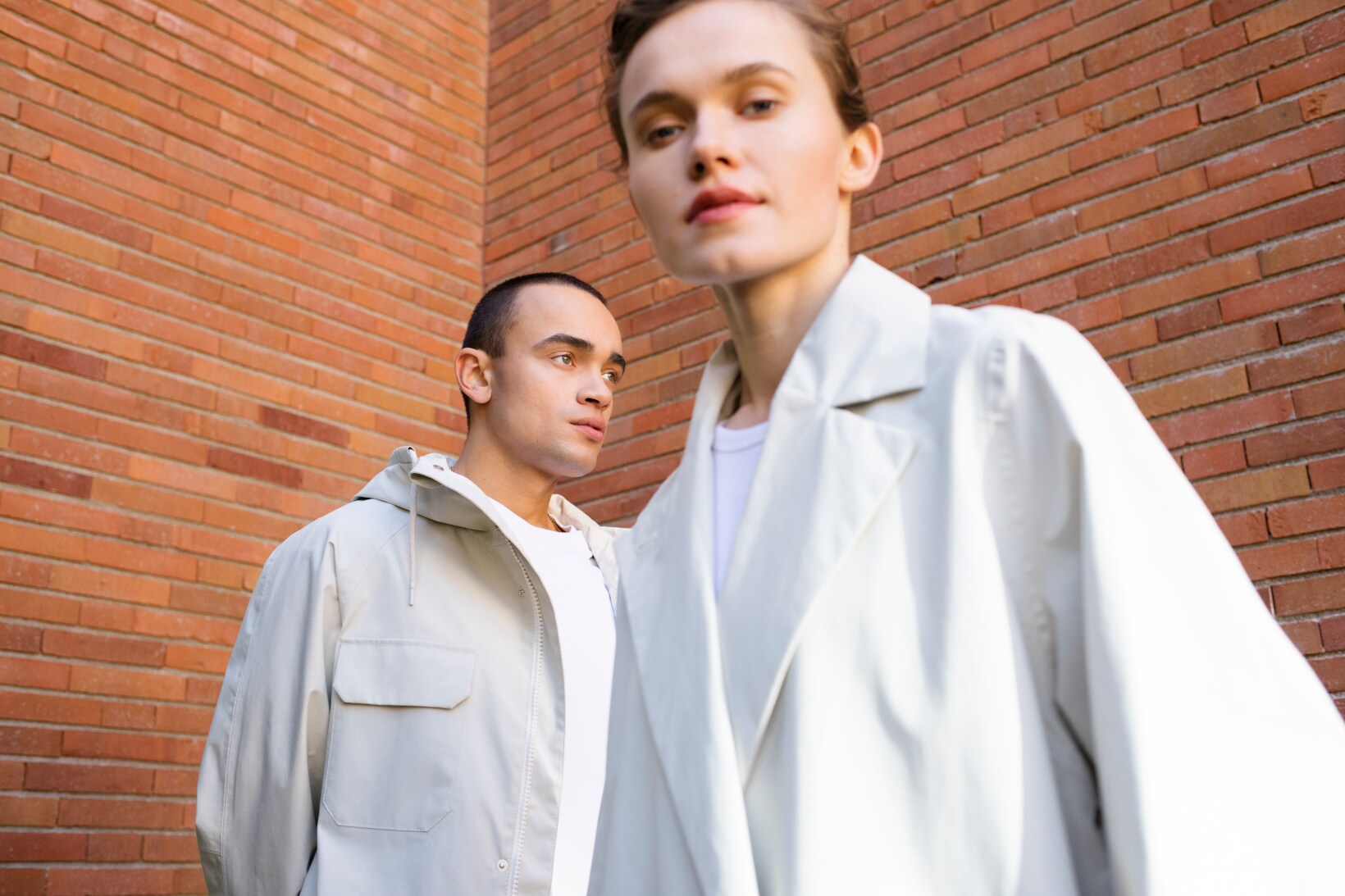 Mann und Frau in weißer Kleidung vor einer Rotklinkerwand.
