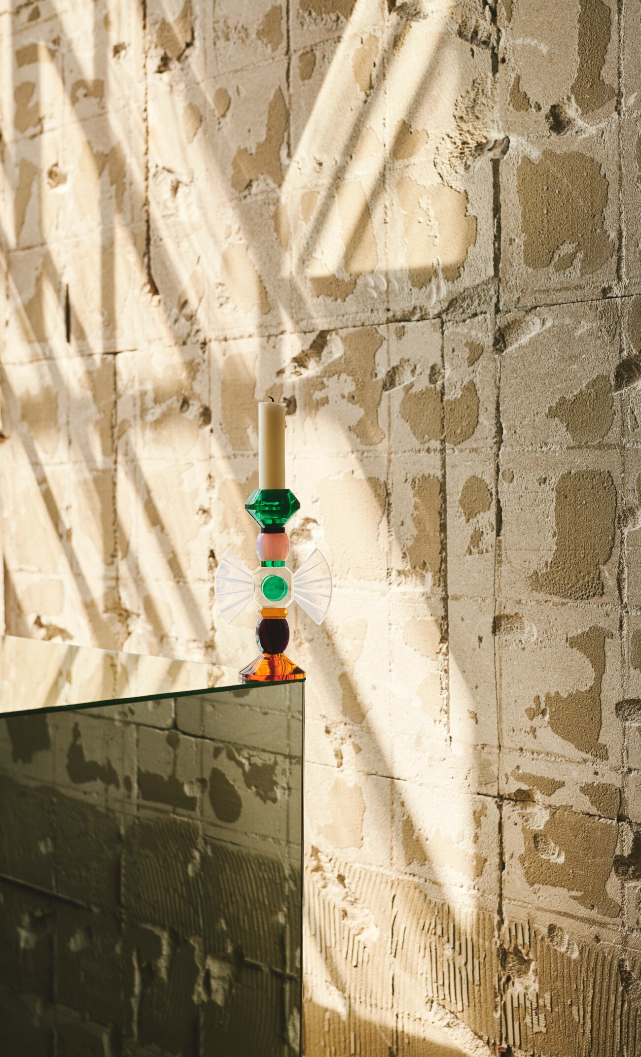 Ein bunter Kerzenständer auf einem eckigen Glastisch vor einer unverputzten Wand Ein bunter Kerzenständer auf einem eckigen Glastisch vor einer unverputzten Wand