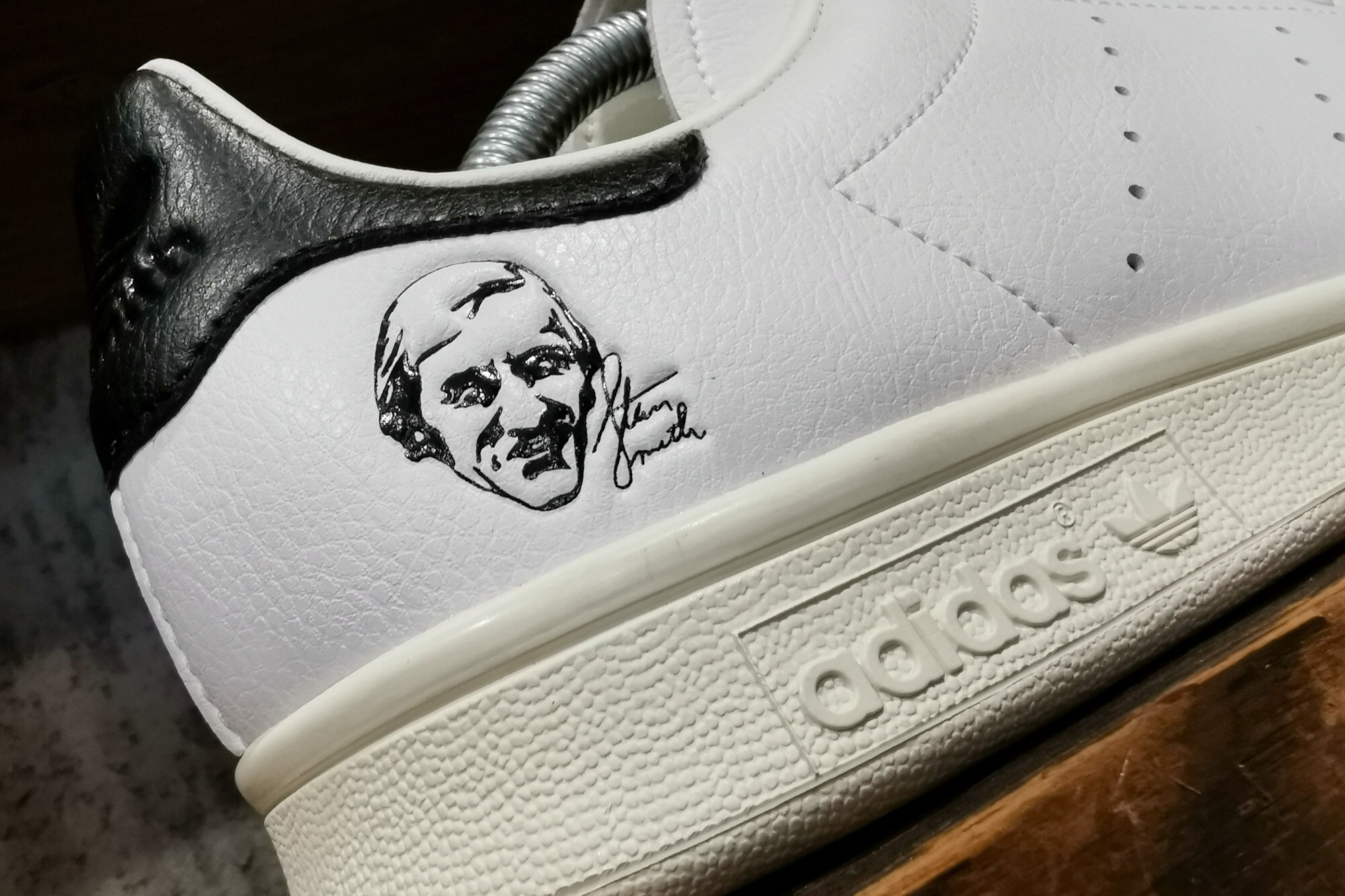 Weiß-schwarzer Adidas-Schuh mit aufgedrucktem Kopf und Schriftzeichen von Stan Smith