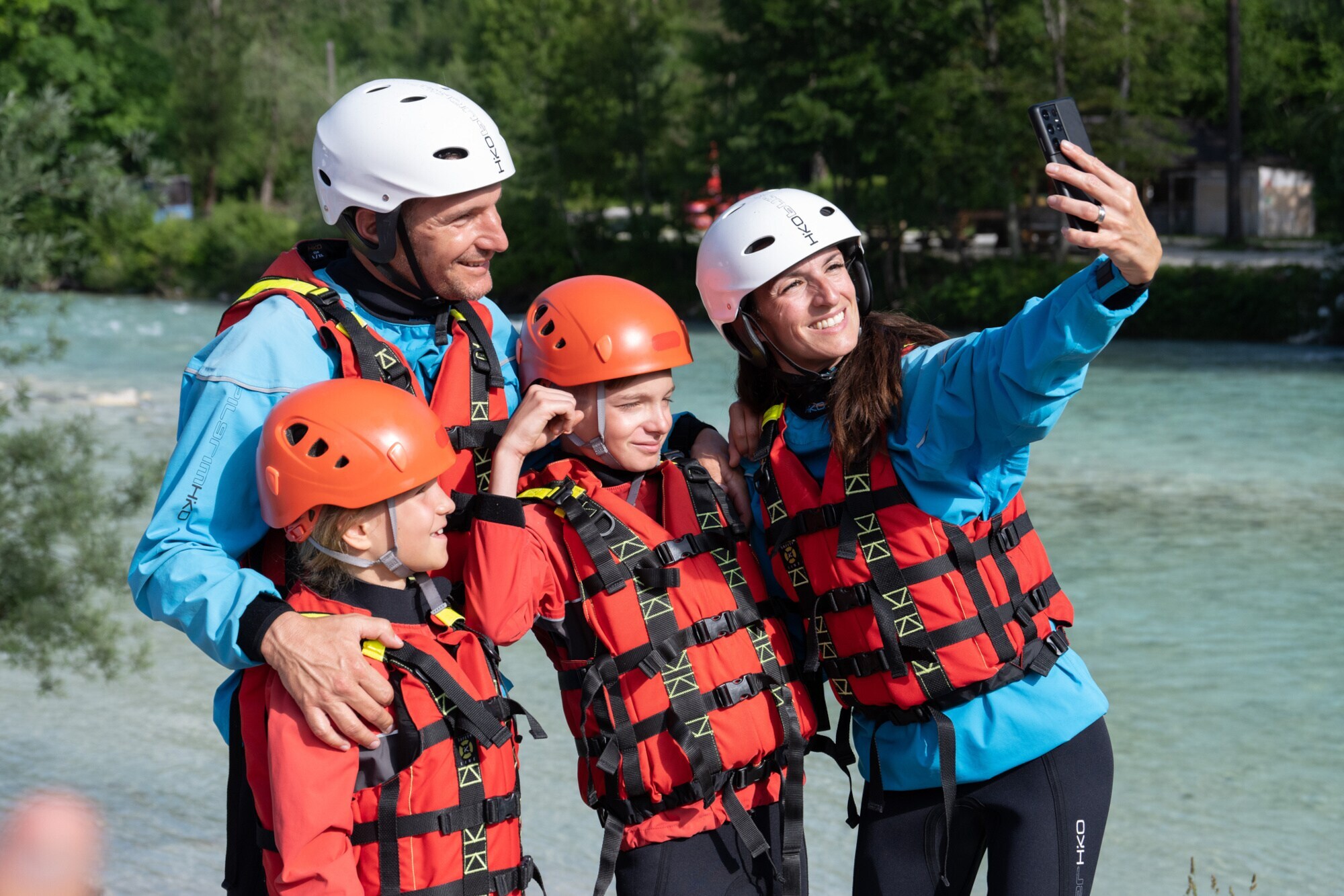 Eine vierköpfige Familie macht ein Selfie in Rafting-Montur vor einem Fluss