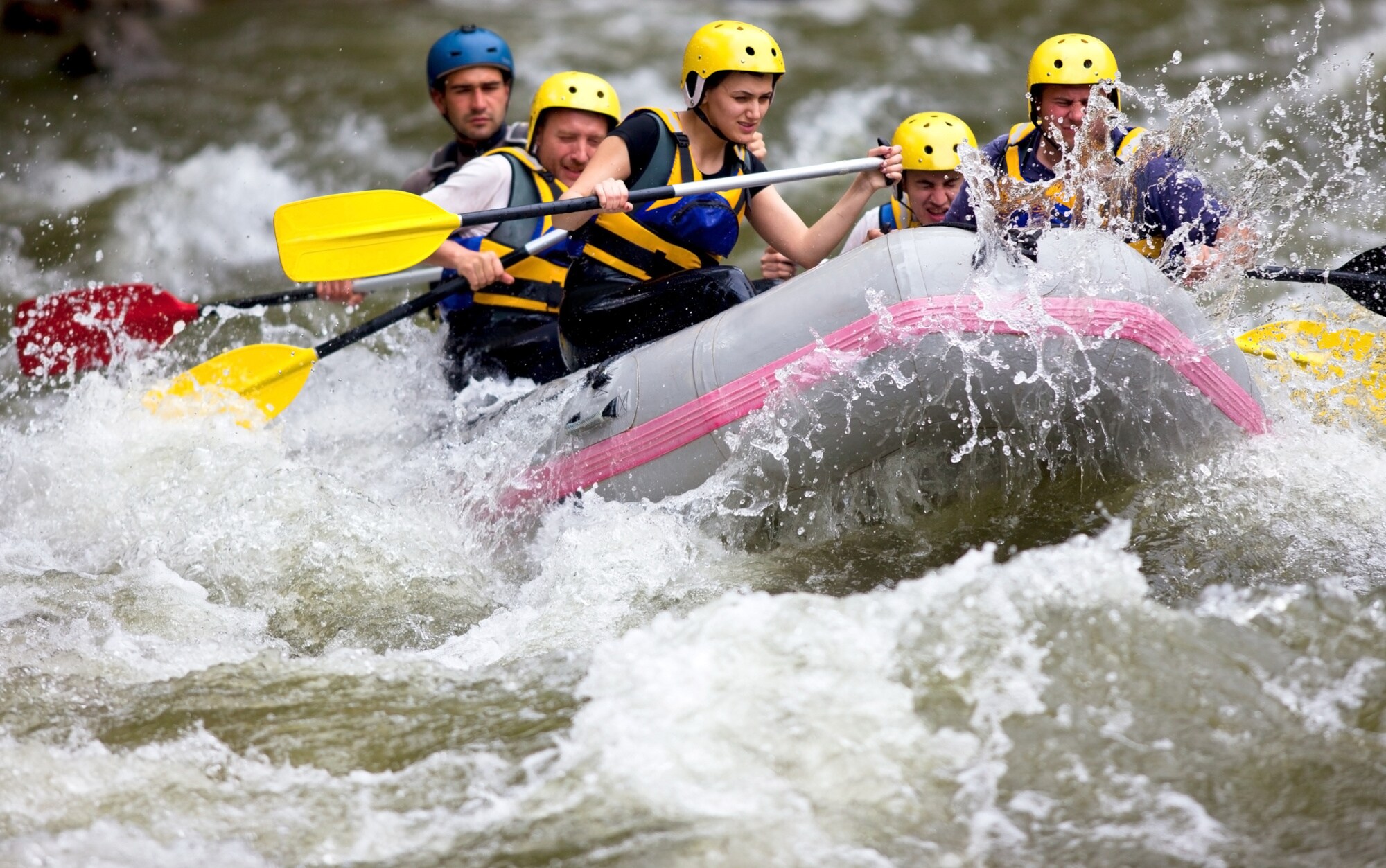 Eine Gruppe von Menschen mit gelben Helmen beim Wildwasser-Rafting auf einem Fluss