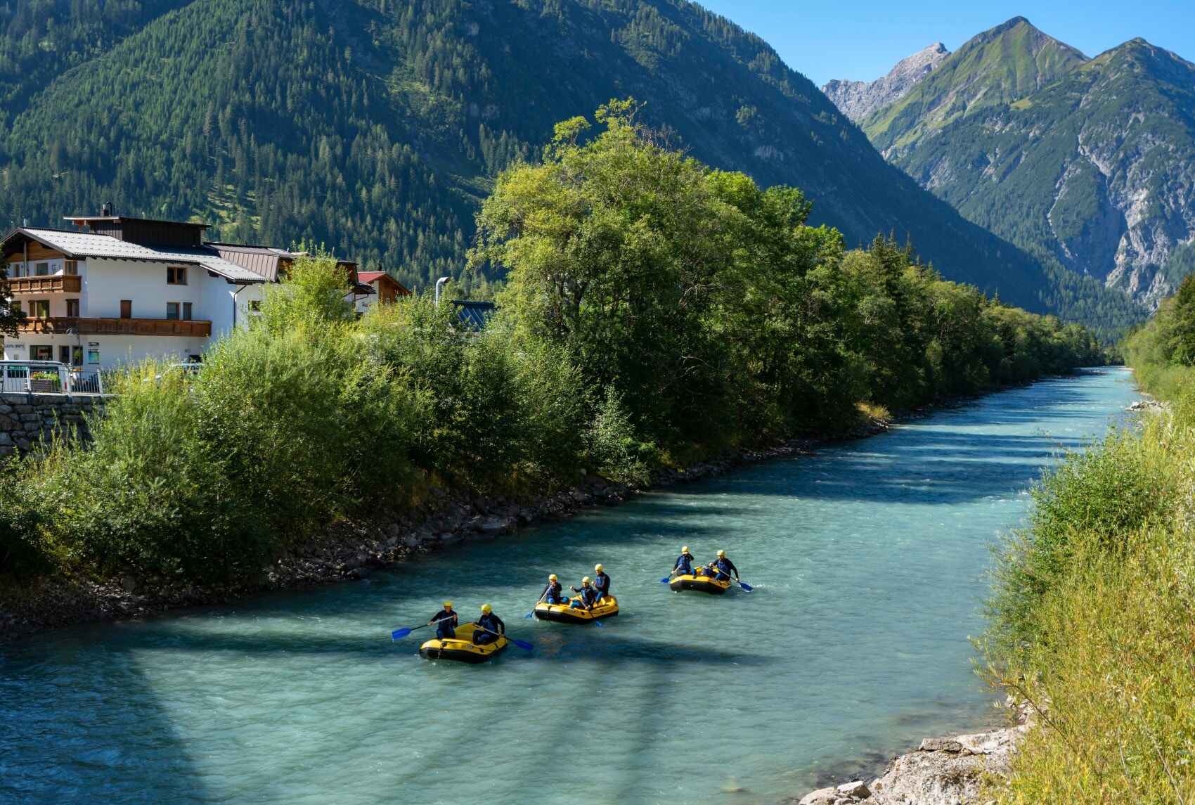 Mehrere Personen fahren in drei gelben Schlauchbooten auf einem Fluss durch eine Berglandschaft Mehrere Personen fahren in drei gelben Schlauchbooten auf einem Fluss durch eine Berglandschaft