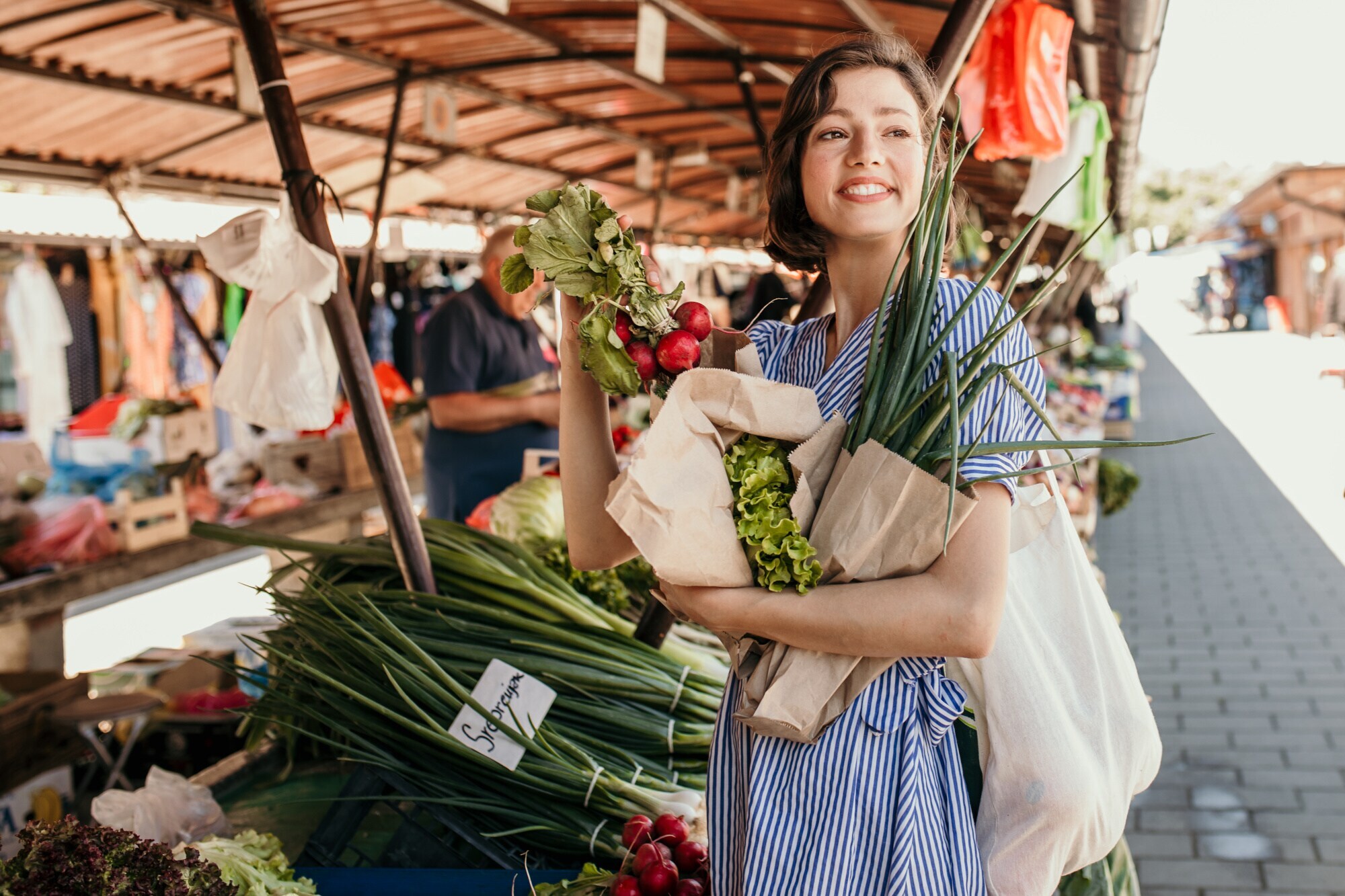 Eine junge Frau kauft auf einem Wochenmarkt regionales Gemüse in Papiertüten ein