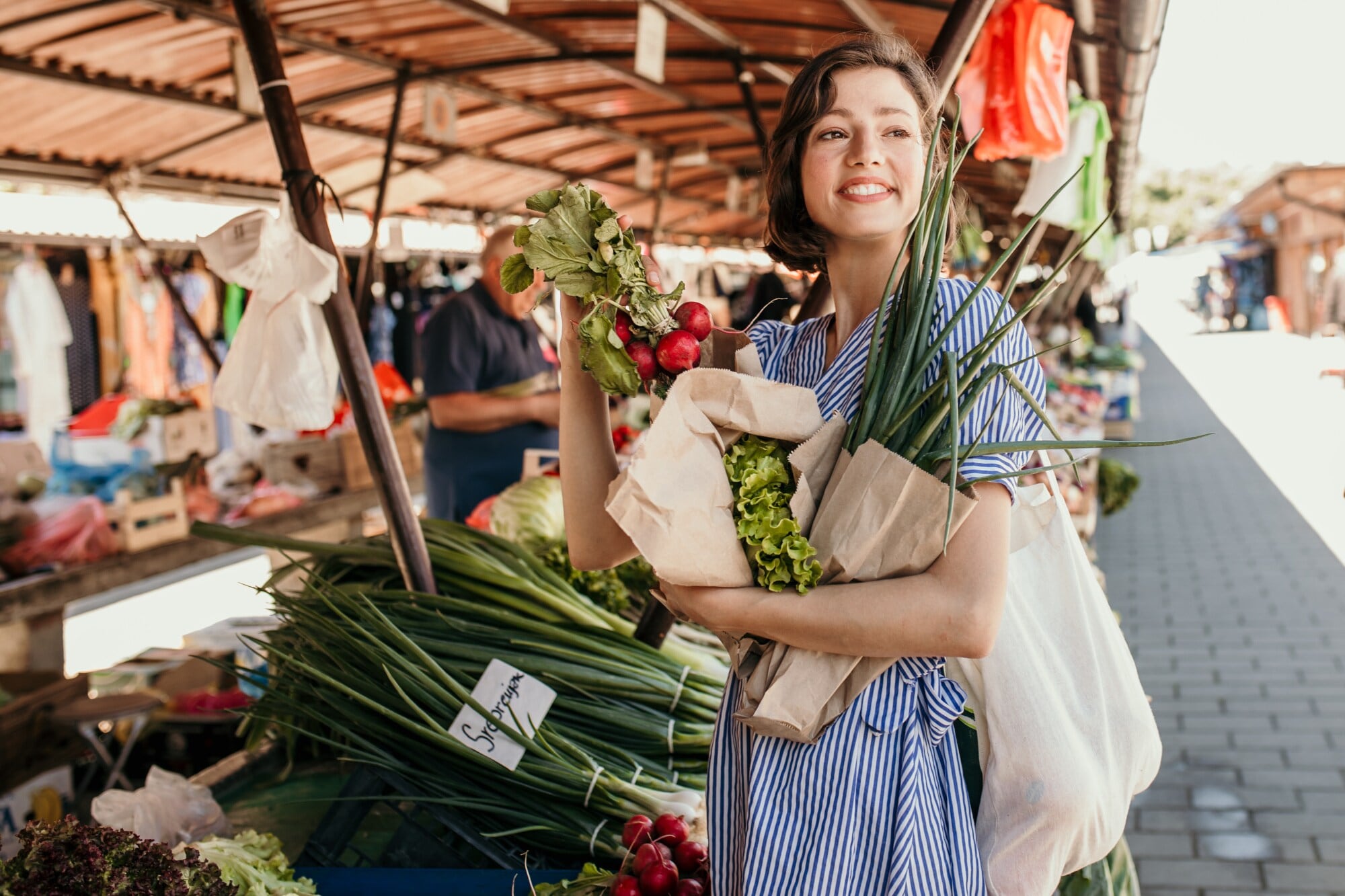 Eine junge Frau kauft auf einem Wochenmarkt regionales Gemüse in Papiertüten ein Eine junge Frau kauft auf einem Wochenmarkt regionales Gemüse in Papiertüten ein