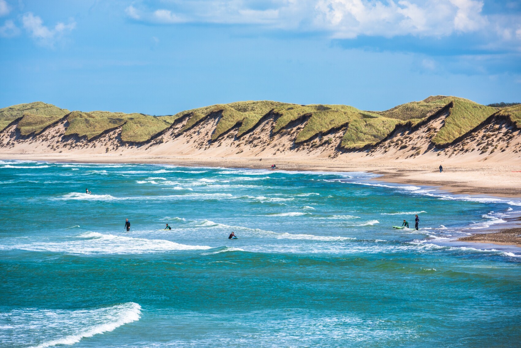 Strandabschnitt der dänischen Nordsee, auf deren Wellen einige Surfer reiten