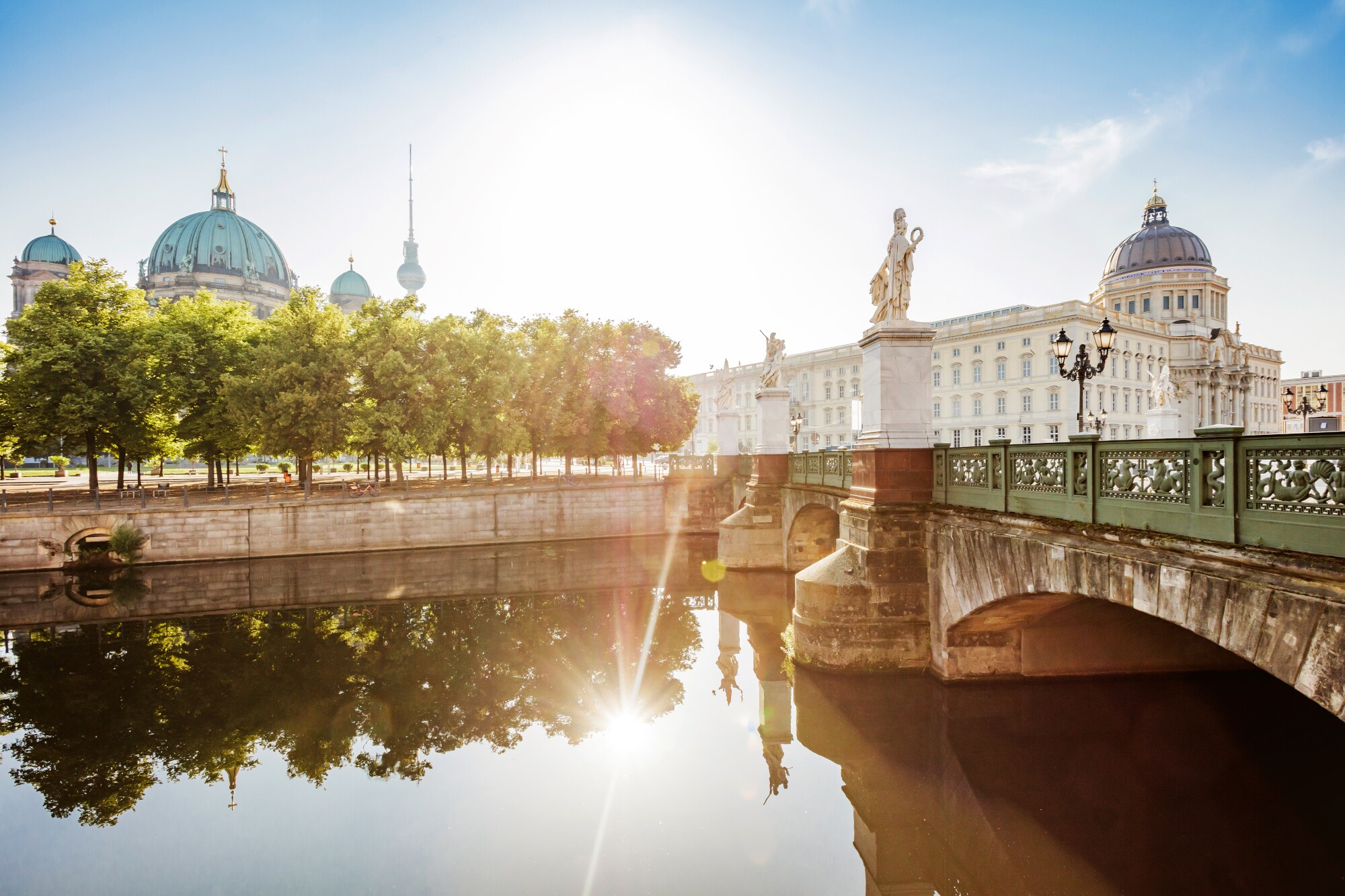 Berliner Dom und Humboldt Forum mit Brücke und Wasser im Vordergrund bei Sonnenschein.
