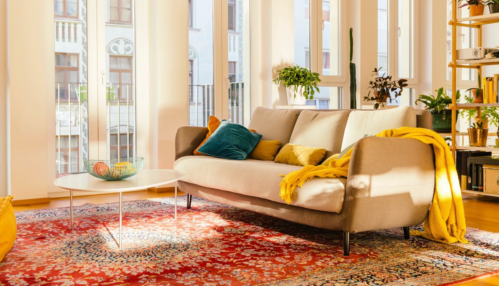 Roter Perserteppich in einer modern eingerichteten Wohnung mit beigefarbener Couch und vor großer Fensterfront