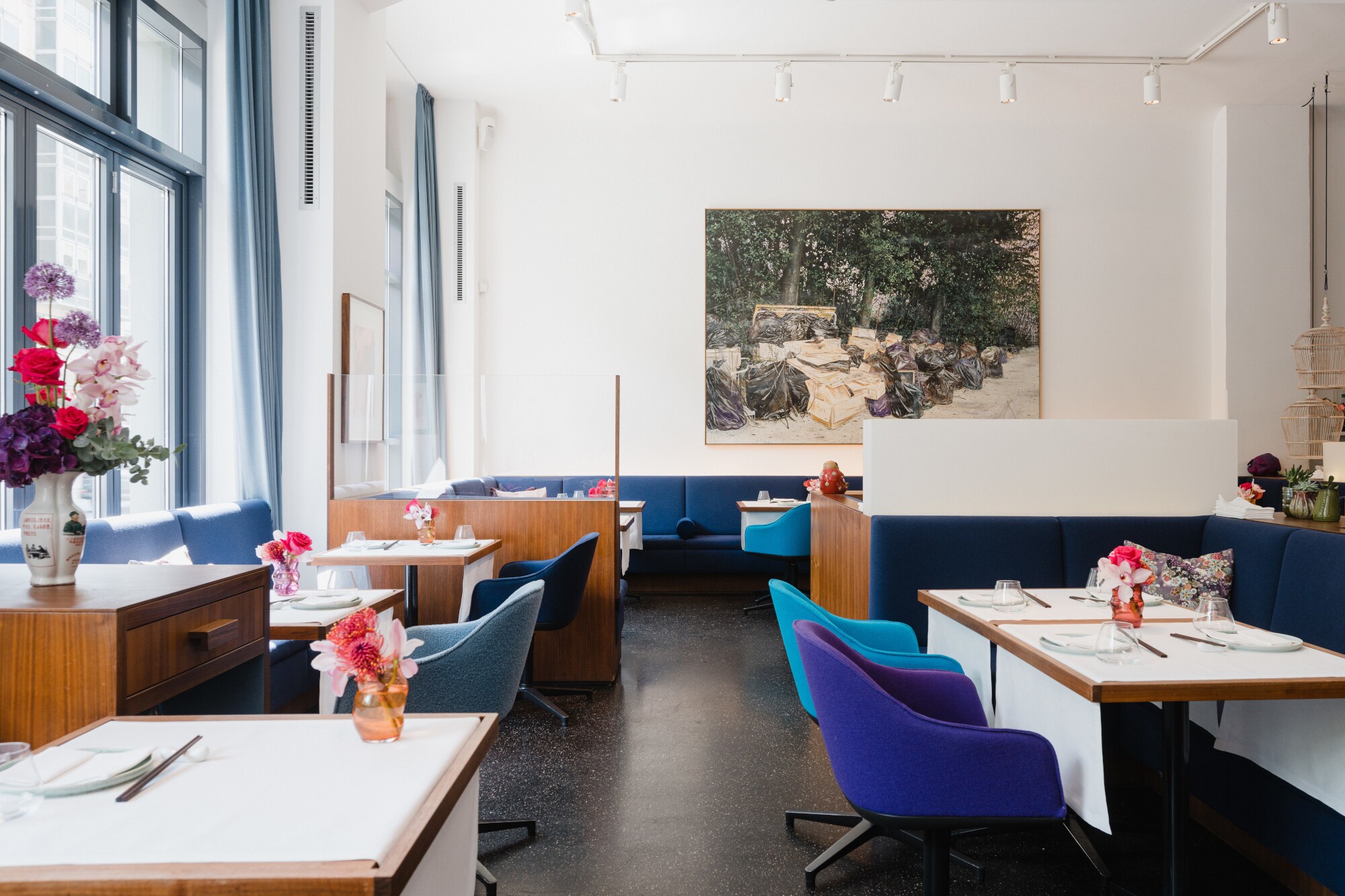 Interieuraufnahme eines modernen, minimalistisch eingerichteten Restaurants mit gedeckten Tischen und Polstermöbeln aus blauem Samt.