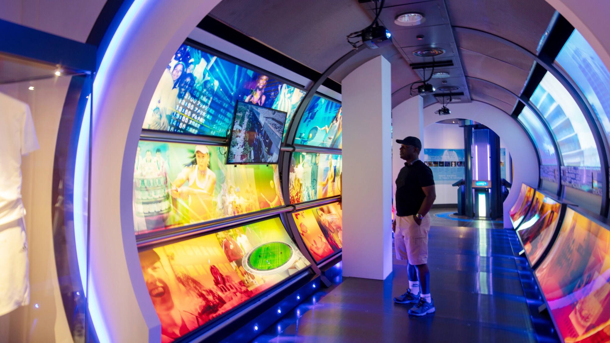 Ein Besucher in einem futuristischen Ausstellungsraum in einem Rundbogen mit digitalen Bildern zum Thema Tennis Ein Besucher in einem futuristischen Ausstellungsraum in einem Rundbogen mit digitalen Bildern zum Thema Tennis