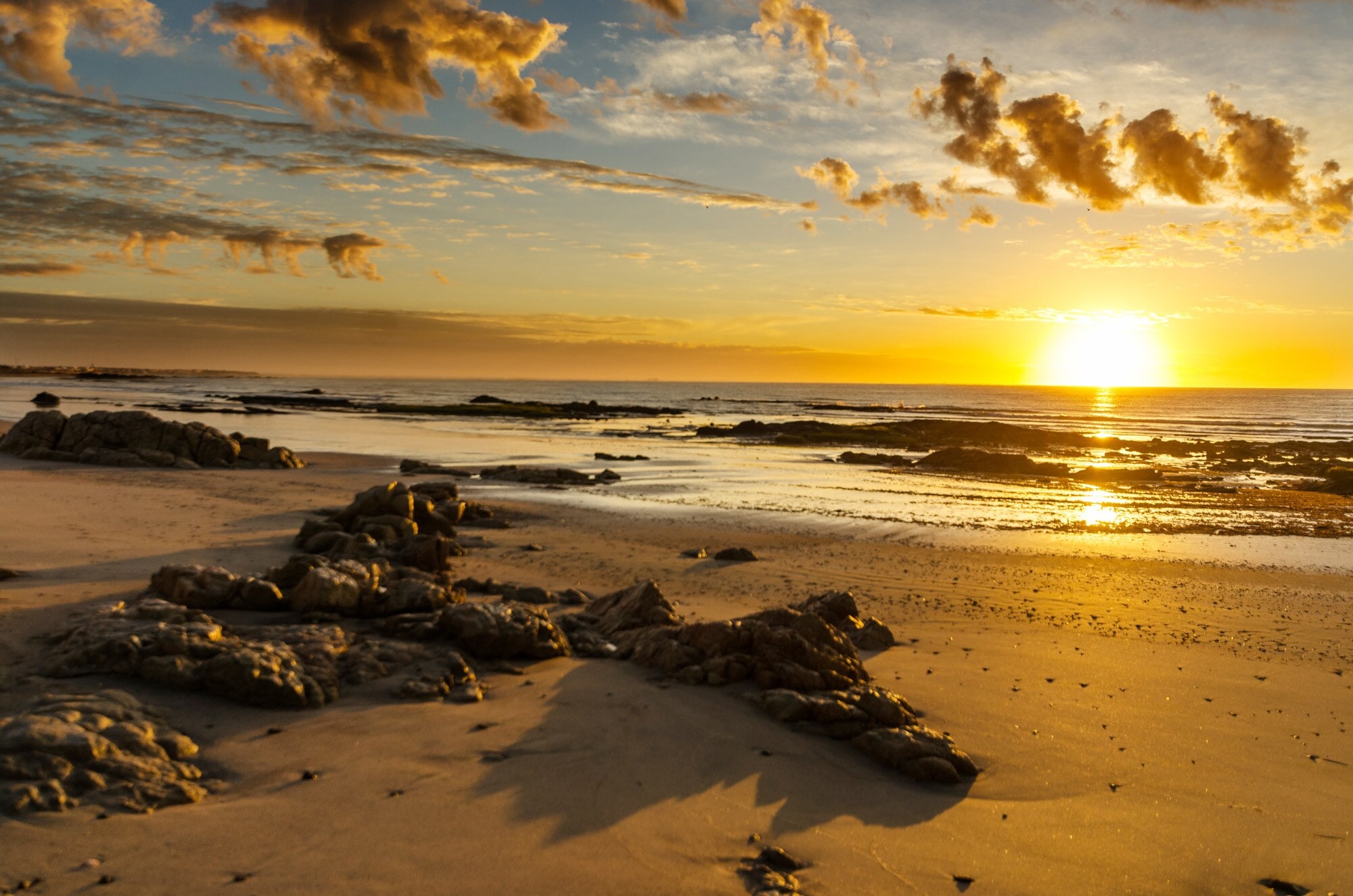 Ein menschenleerer, teilweise felsiger Sandstrand mit Sonnenuntergang über dem Meer Ein menschenleerer, teilweise felsiger Sandstrand mit Sonnenuntergang über dem Meer