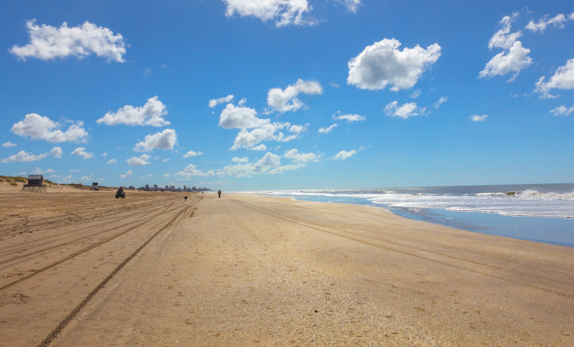 Panoramaaufnahme eines weitläufigen Sandstrandes unter blauem Himmel mit vereinzelten Kumuluswolken