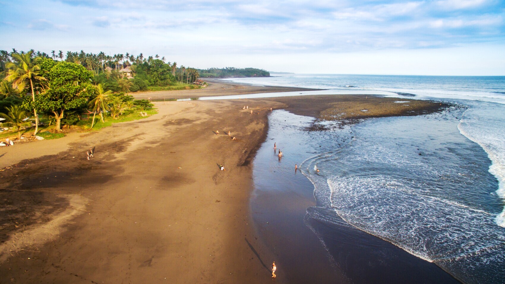 Weitläufiger, naturbelassener Strand mit dunklem Sand und vereinzelten Badegästen