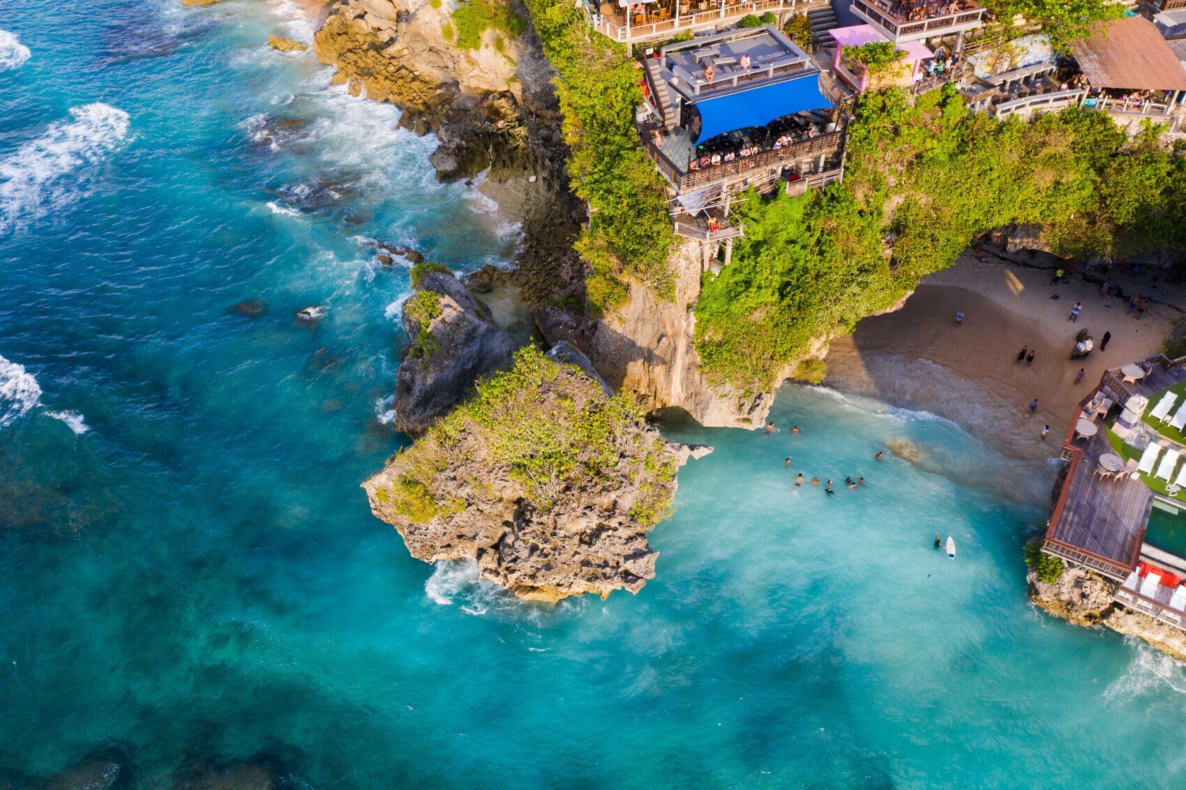 Luftaufnahme eines kleinen Sandstrandes, versteckt in einer Felsbucht, umgeben von Restaurants