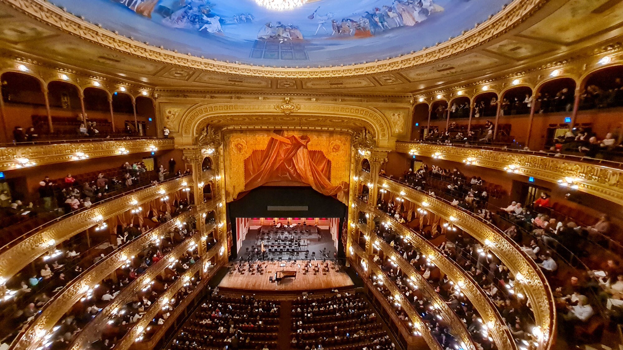 Colon Theater Klavierkonzert mit Publikum in einem prachtvollen, runden Opernsaal mit Goldverzierungen, roten Sesseln und blauem Deckenfresko Klavierkonzert mit Publikum in einem prachtvollen, runden Opernsaal mit Goldverzierungen, roten Sesseln und blauem Deckenfresko