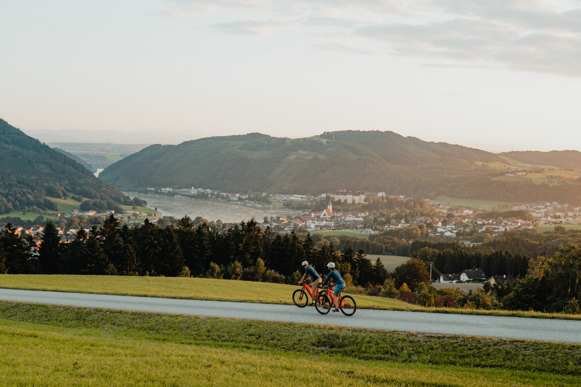 Zwei Radfahrer fahren auf dem Donauradweg mit Blick auf Berge