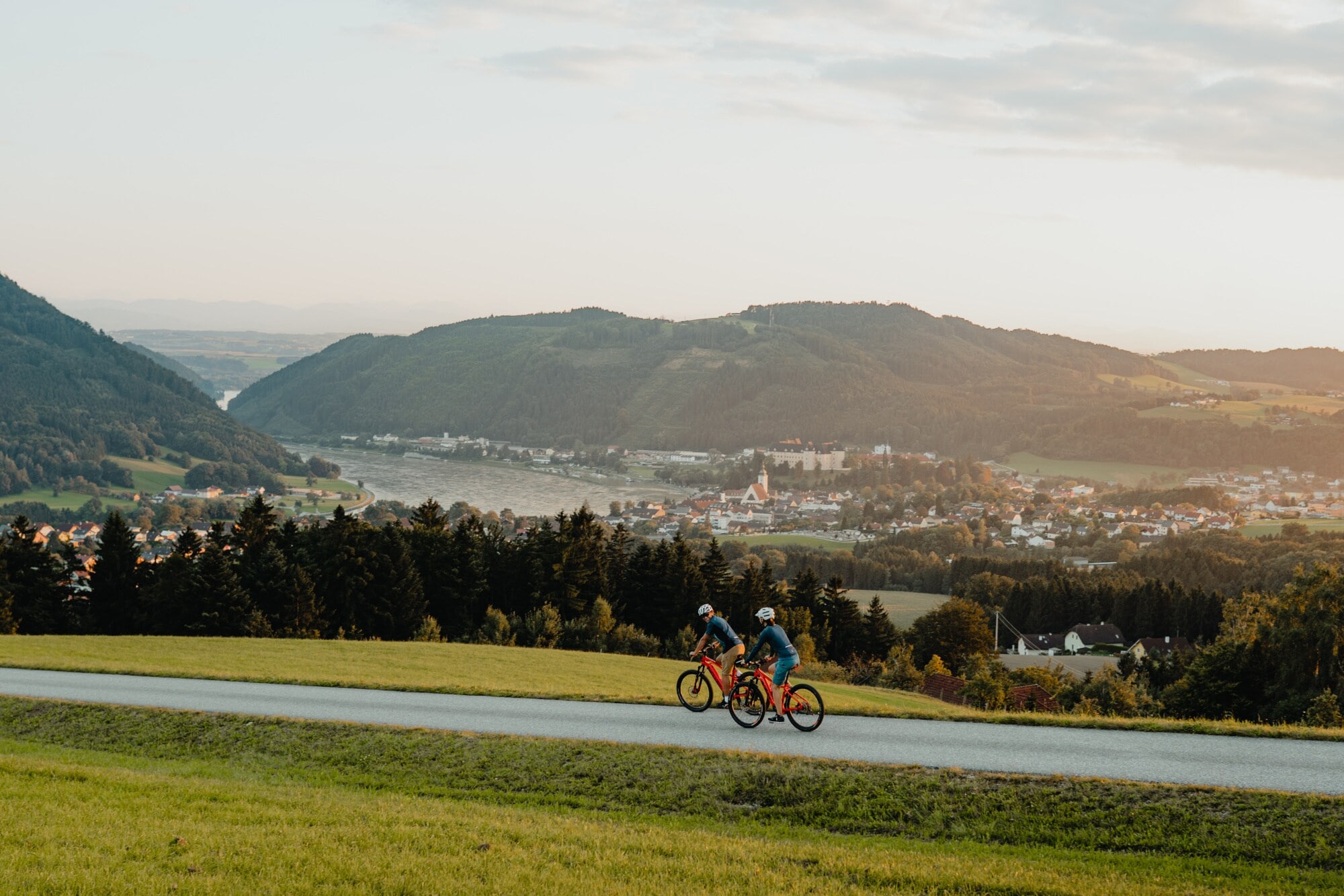 Zwei Radfahrer fahren auf dem Donauradweg mit Blick auf Berge Zwei Radfahrer fahren auf dem Donauradweg mit Blick auf Berge