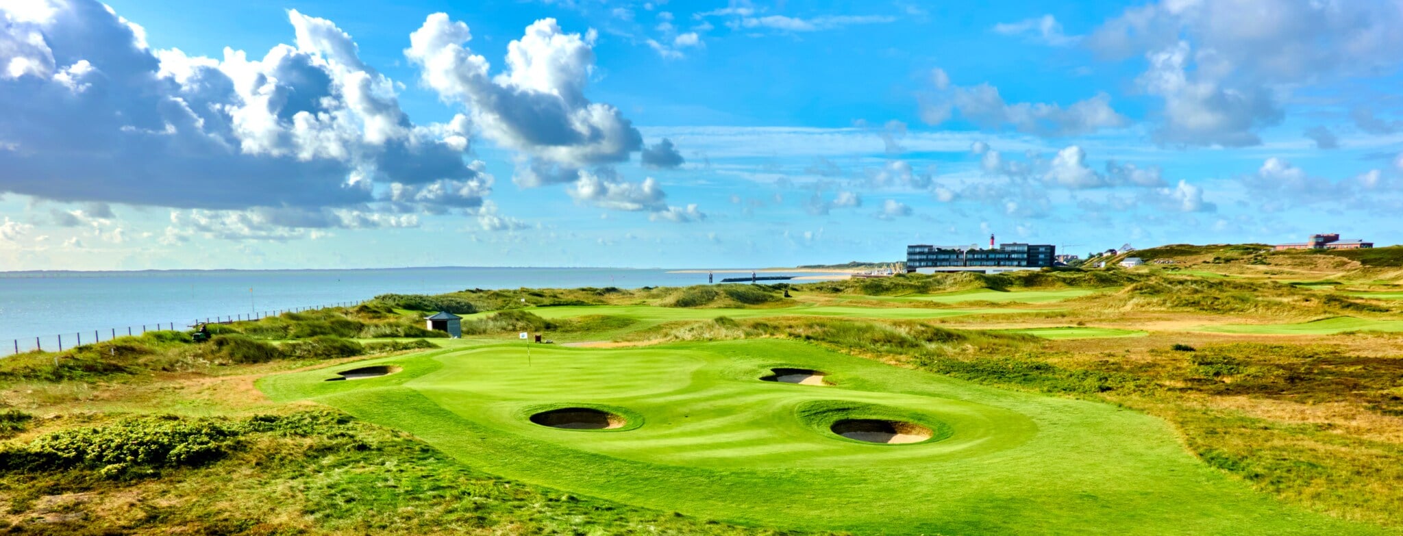 Grüner Golfplatz mit runden Bunkern mit Hotel und Meer im Hintergrund Grüner Golfplatz mit runden Bunkern mit Hotel und Meer im Hintergrund