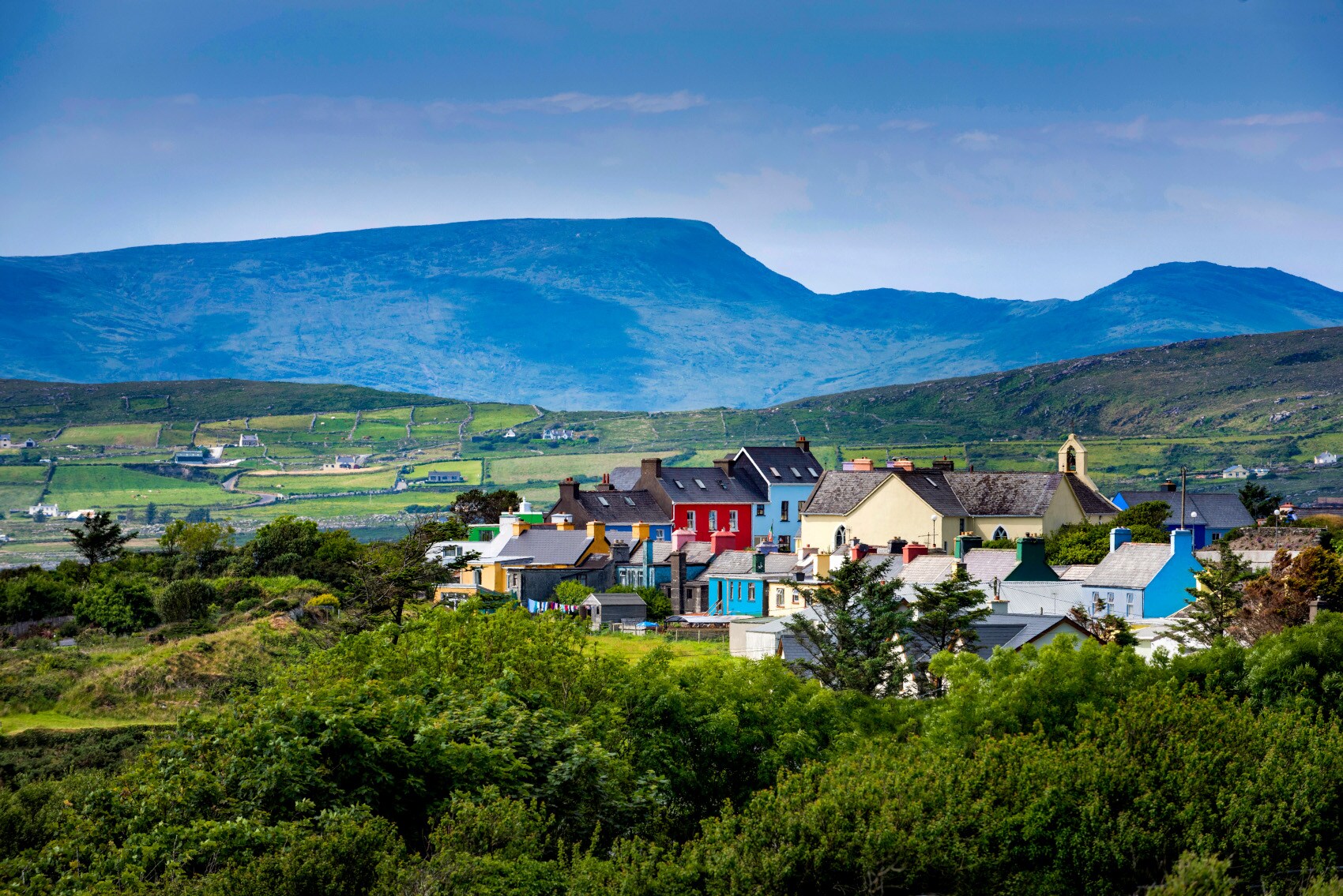 Kleine Ortschaft mit bunten Häusern inmitten einer grünen Hügellandschaft Kleine Ortschaft mit bunten Häusern inmitten einer grünen Hügellandschaft
