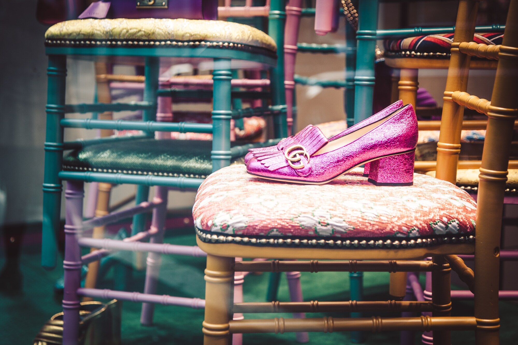 Ein Paar glitzernde, pinkfarbene Loafer mit goldenem Gucci-Logo steht auf einem Stuhl in einem Schaufenster
