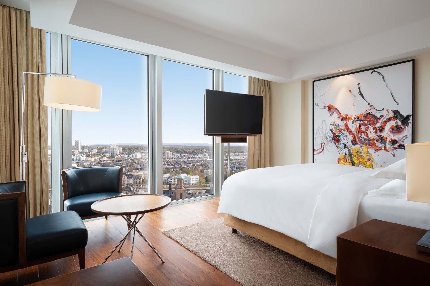 Eine moderne, helle Hotelsuite mit bodentiefen Fenstern und Panoramablick auf Frankfurt am Main