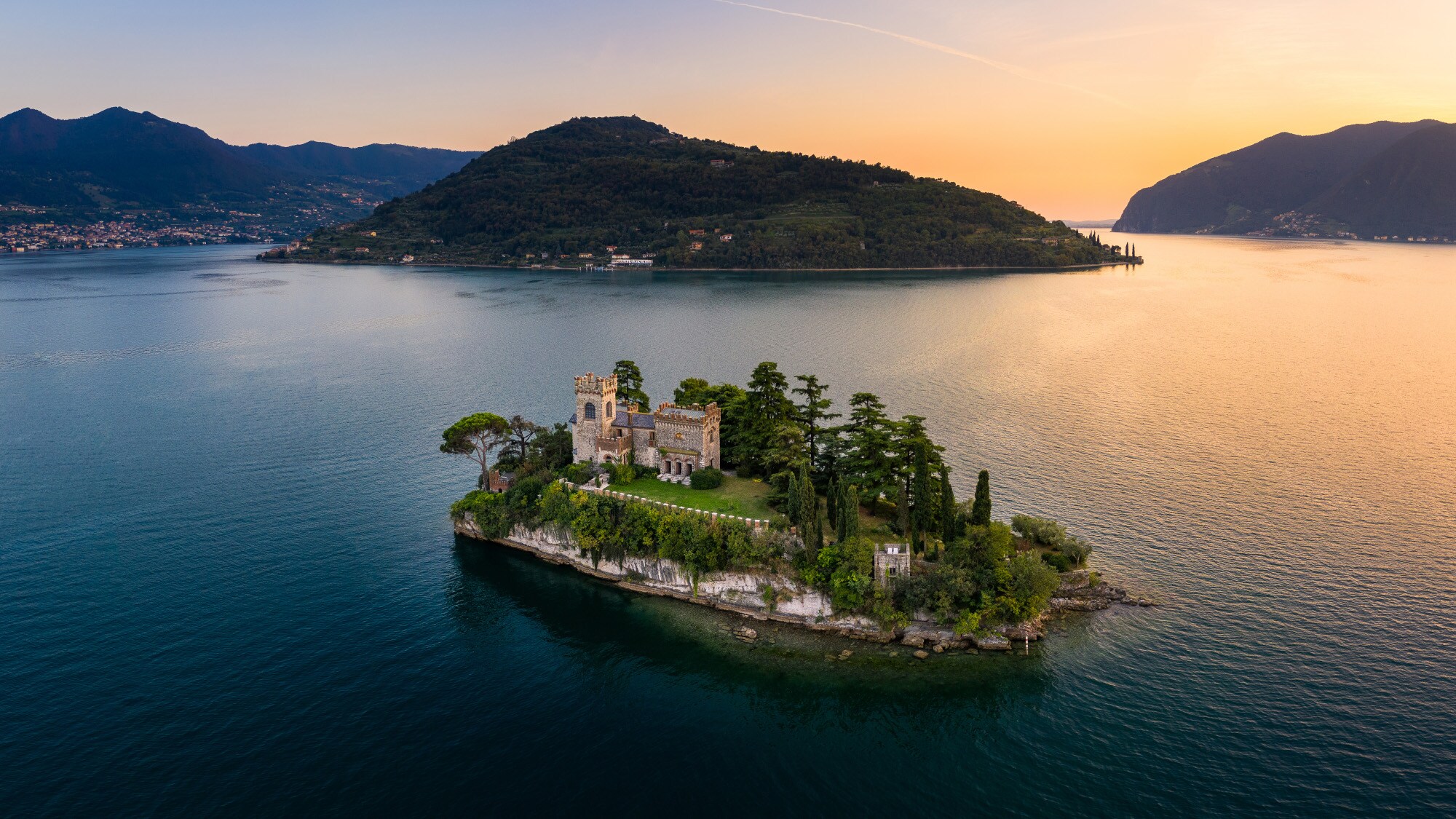 Luftaufnahme einer kleinen Felsinsel mit Burg und Bäumen in einem großen See bei Sonnenuntergang Luftaufnahme einer kleinen Felsinsel mit Burg und Bäumen in einem großen See bei Sonnenuntergang