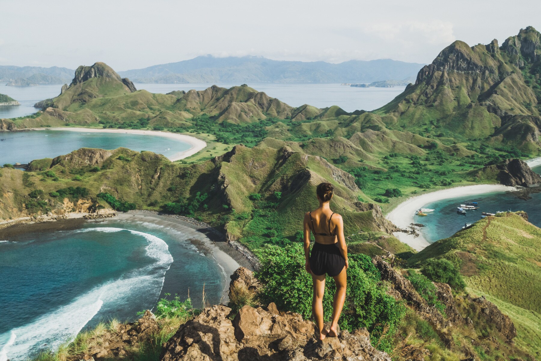 Eine Person steht auf einem Felsvorsprung und blickt über einen Teil des Komodo-Nationalparks mit kleinen Bergen und Buchten