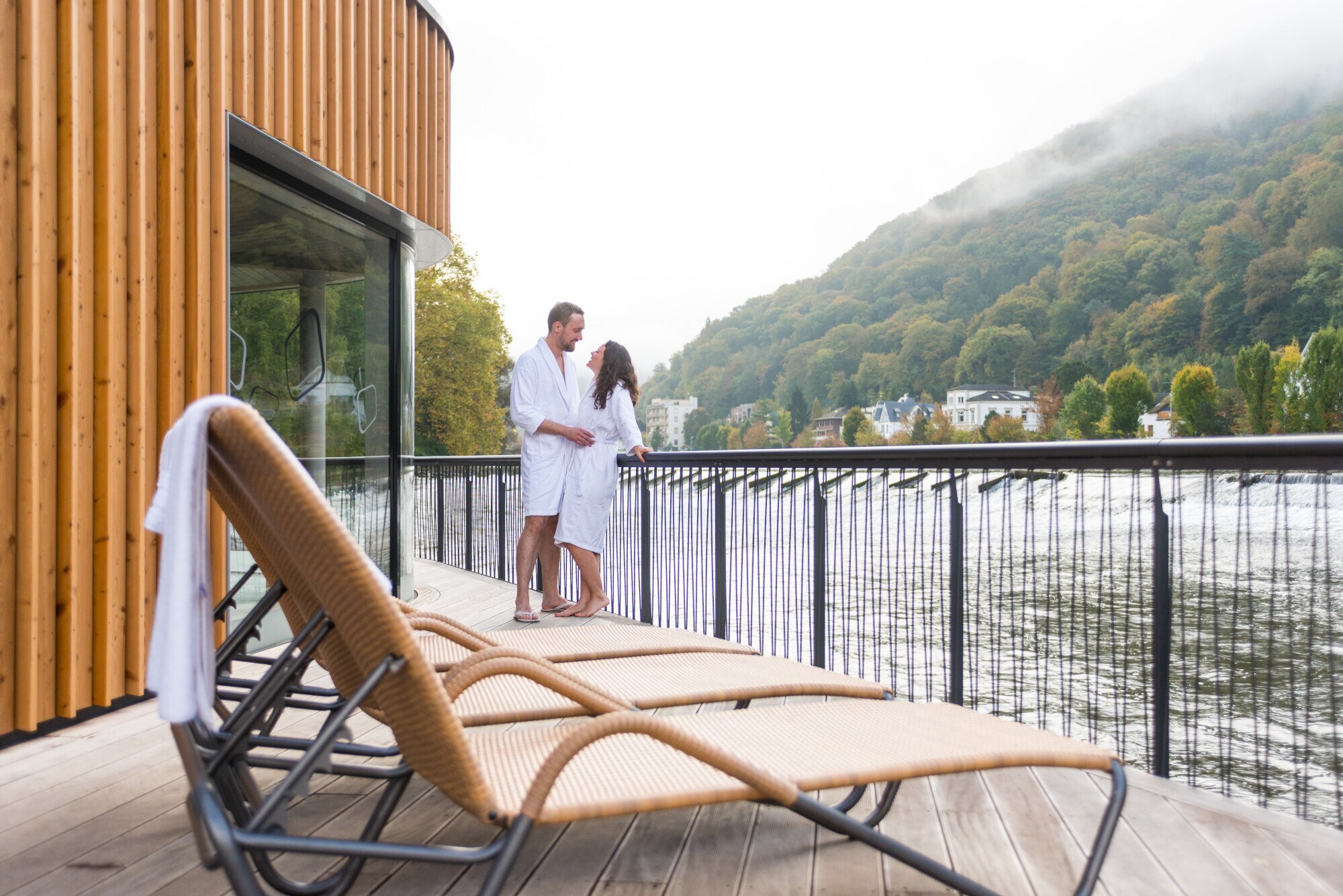Ein Mann und eine Frau in weißen Bademänteln stehen auf dem Sonnendeck einer Flusssauna