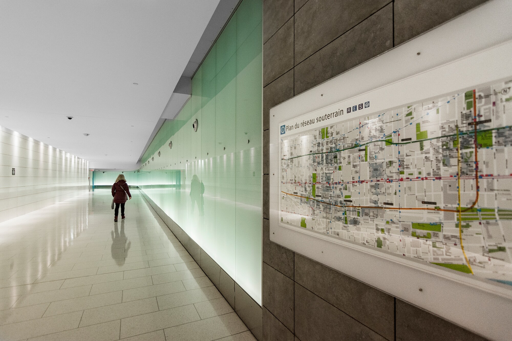 Eine Person läuft in einem hell erleuchteten Gang, an der Seite ist ein Plan der unterirdischen Stadt Montreals zu sehen