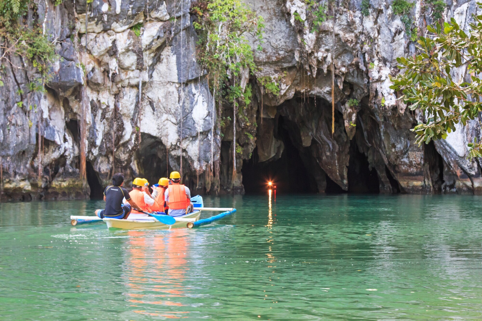 Ein kleines Ausflugsboot mit Menschen auf einem Gewässer mit Steinhöhlen Ein kleines Ausflugsboot mit Menschen auf einem Gewässer mit Steinhöhlen