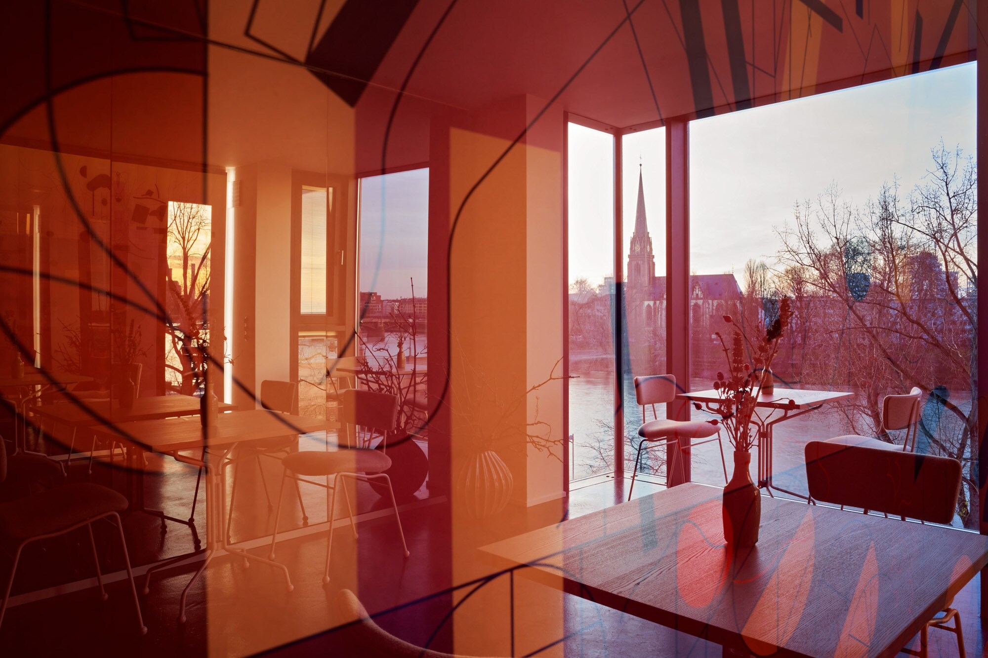 Tische und Stühle im Restaurant Seven Swans vor einem großen Fenster mit Blick auf den Main