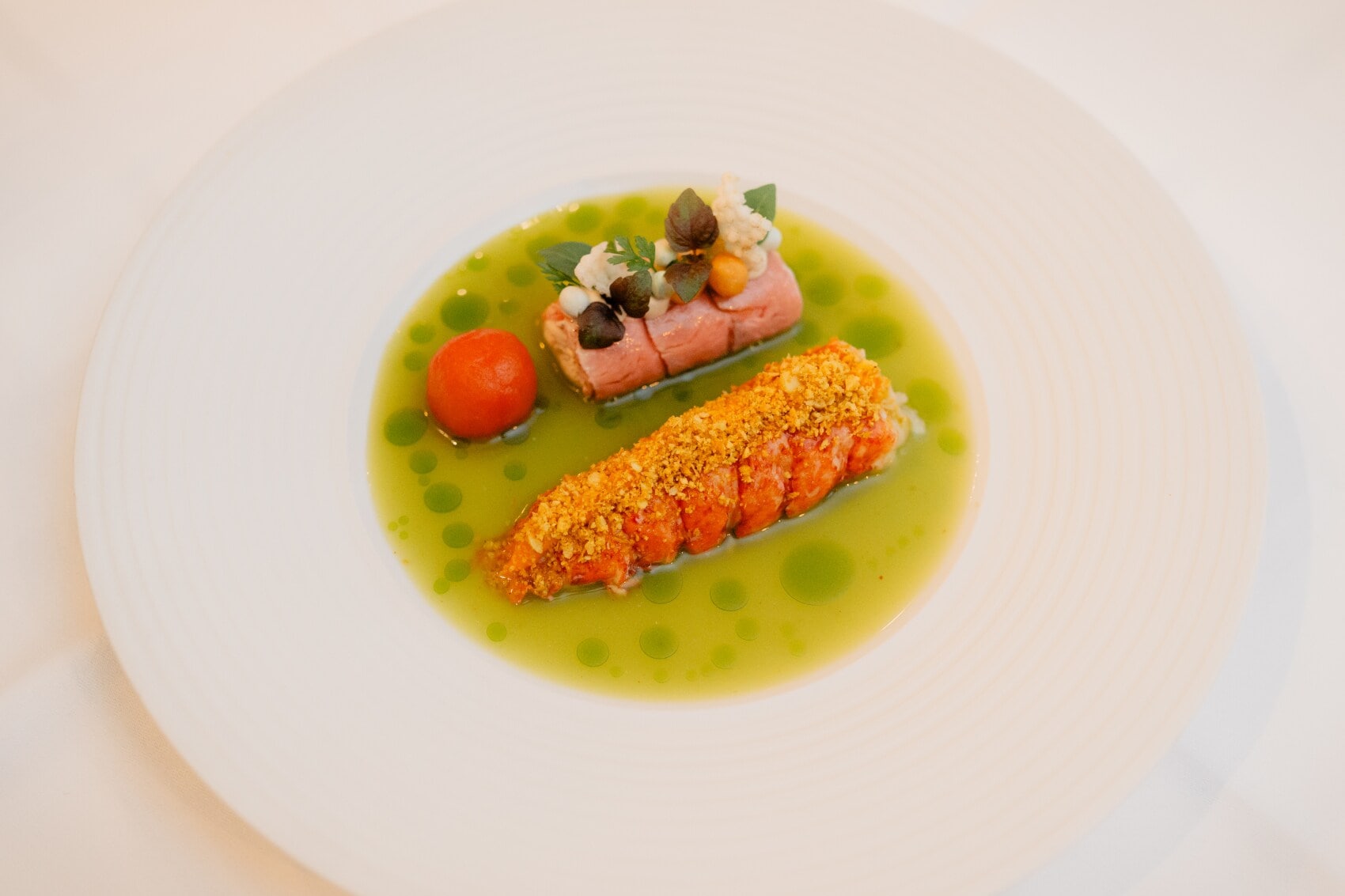 Ein reduziertes Gourmet-Gerichts mit grüner Soße und einer Tomate auf einem weißem Porzellanteller Ein reduziertes Gourmet-Gerichts mit grüner Soße und einer Tomate auf einem weißem Porzellanteller