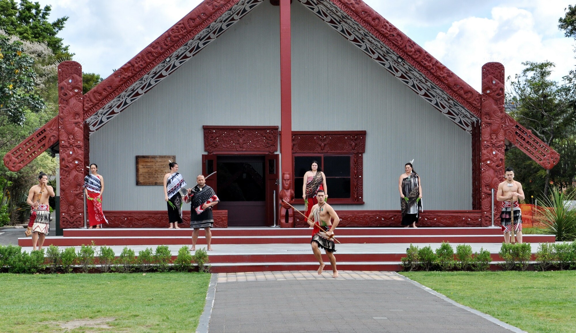 Ein Gruppe Maori bei einer Tanzvorführung vor einem traditionellen Maori Haus.