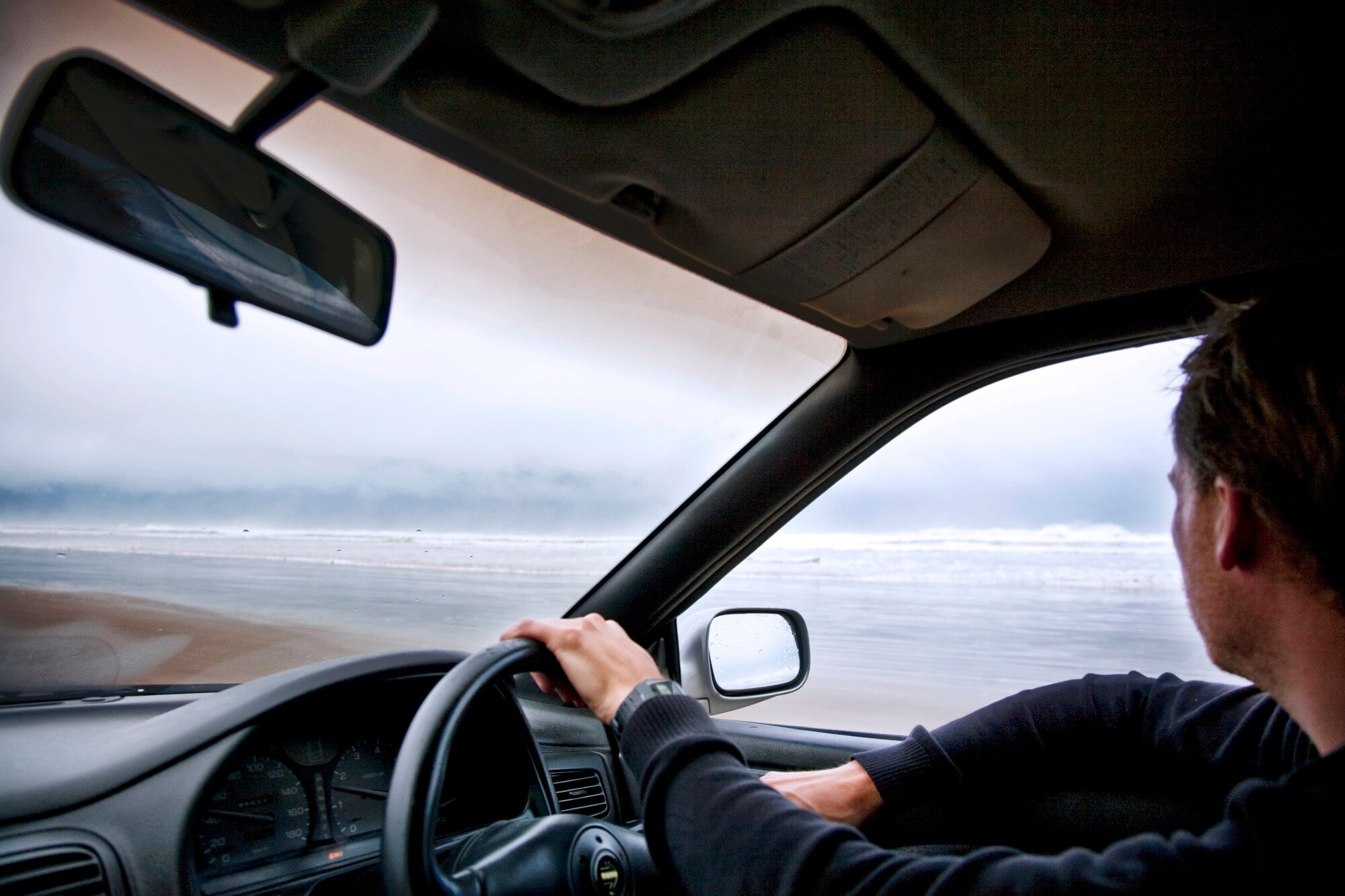Person im Profil am Steuer eines rechtsgelenkten Autos an einem nebeligen Strand. Person im Profil am Steuer eines rechtsgelenkten Autos an einem nebeligen Strand.