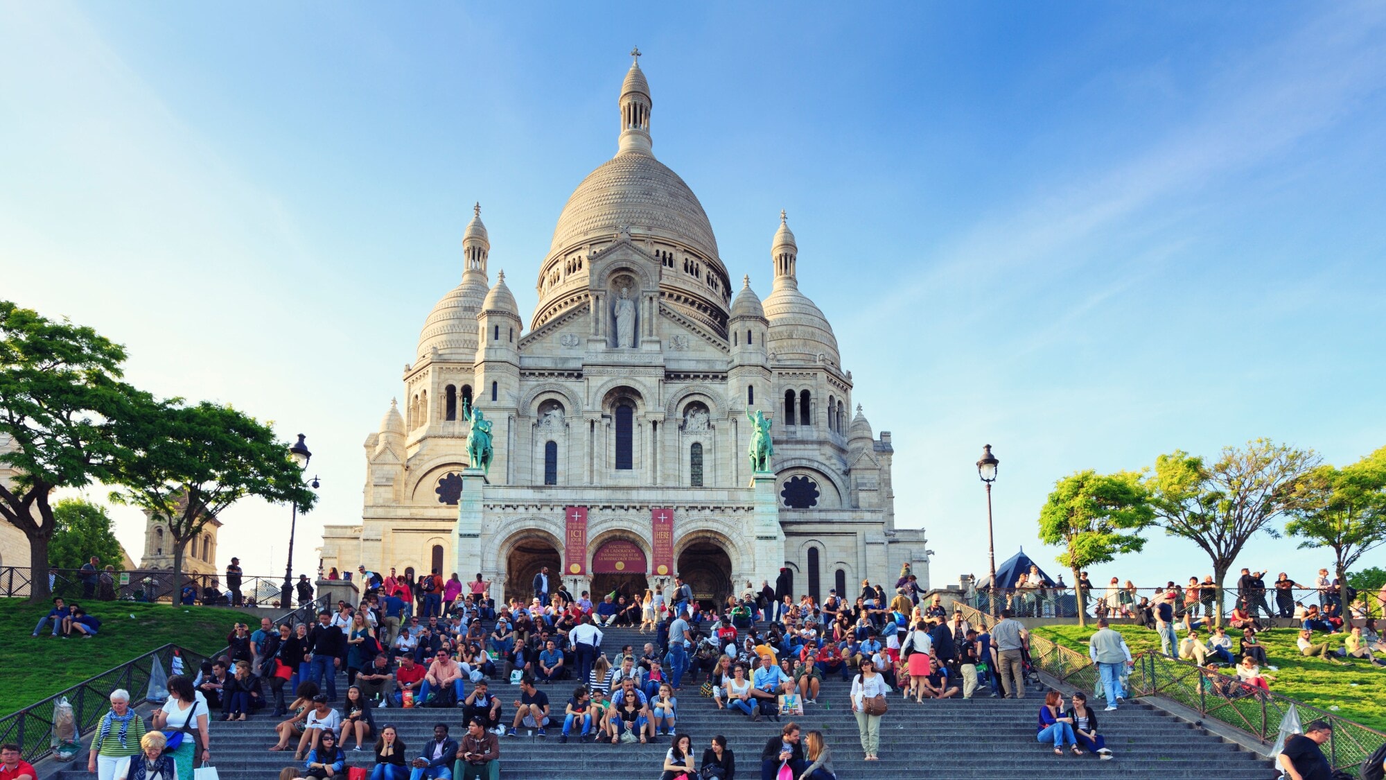 Sitzende Personen auf einer Treppe vor der Wallfahrtskirche Sacré-Coeur auf einem Hügel. Sitzende Personen auf einer Treppe vor der Wallfahrtskirche Sacré-Coeur auf einem Hügel.