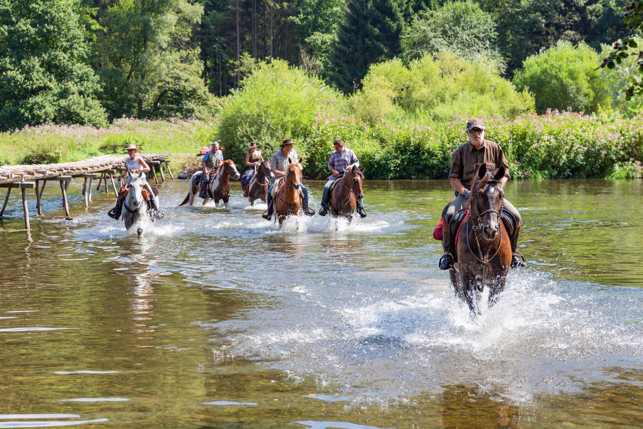 Eine Personengruppe durchquert auf Pferden einen Fluss