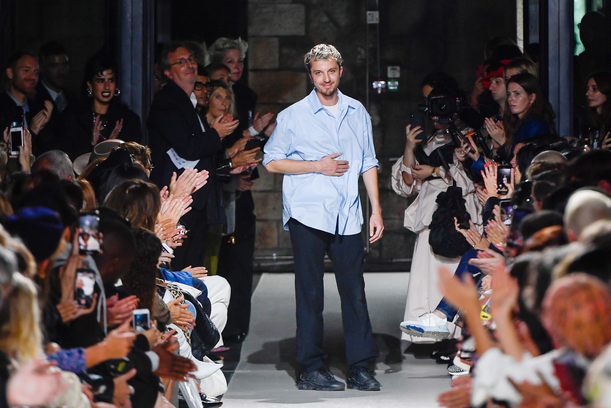 Designer Glenn Martens steht am Ende eines Laufstegs vor applaudierendem Publikum