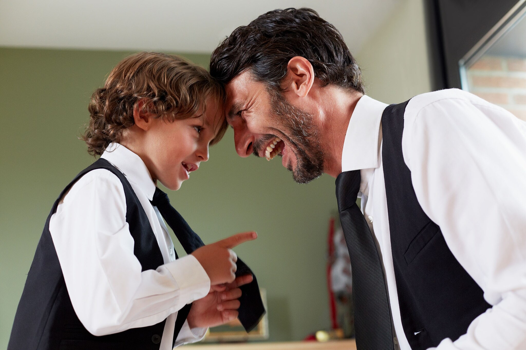 Ein Vater und sein kleiner Sohn im Partnerlook mit weißem Hemd und schwarzer Krawatte stehen sich lachend gegenüber.