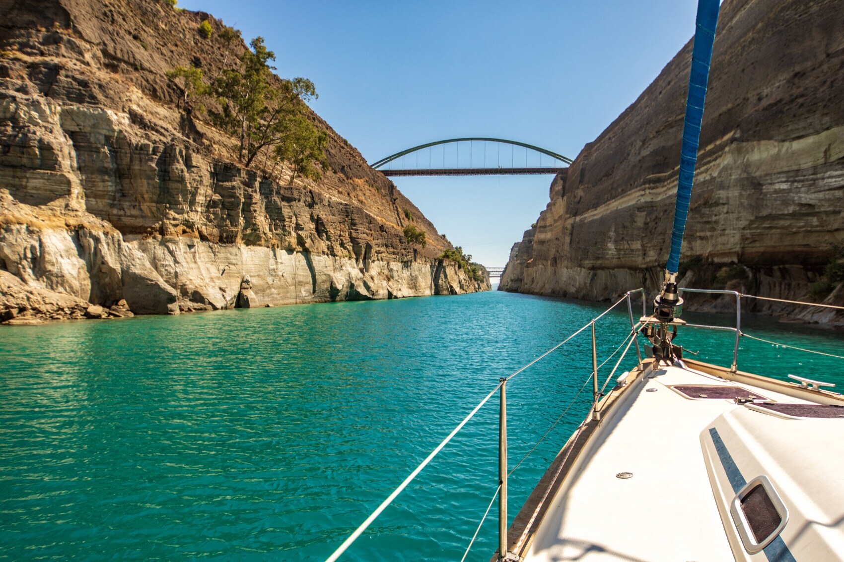 Kanal von Korinth mit einer von steilen Felswänden eingerahmten Wasserstraße, im Vordergrund der Bug eines Segelbootes Kanal von Korinth mit einer von steilen Felswänden eingerahmten Wasserstraße, im Vordergrund der Bug eines Segelbootes