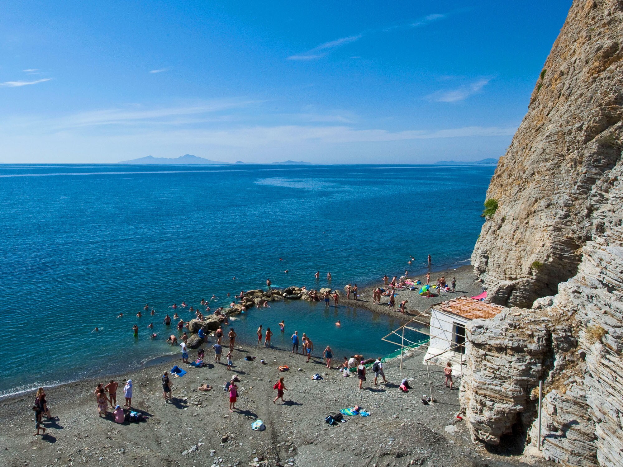 Personen baden in einem natürlichen Wasserbecken an einem Kiesstrand