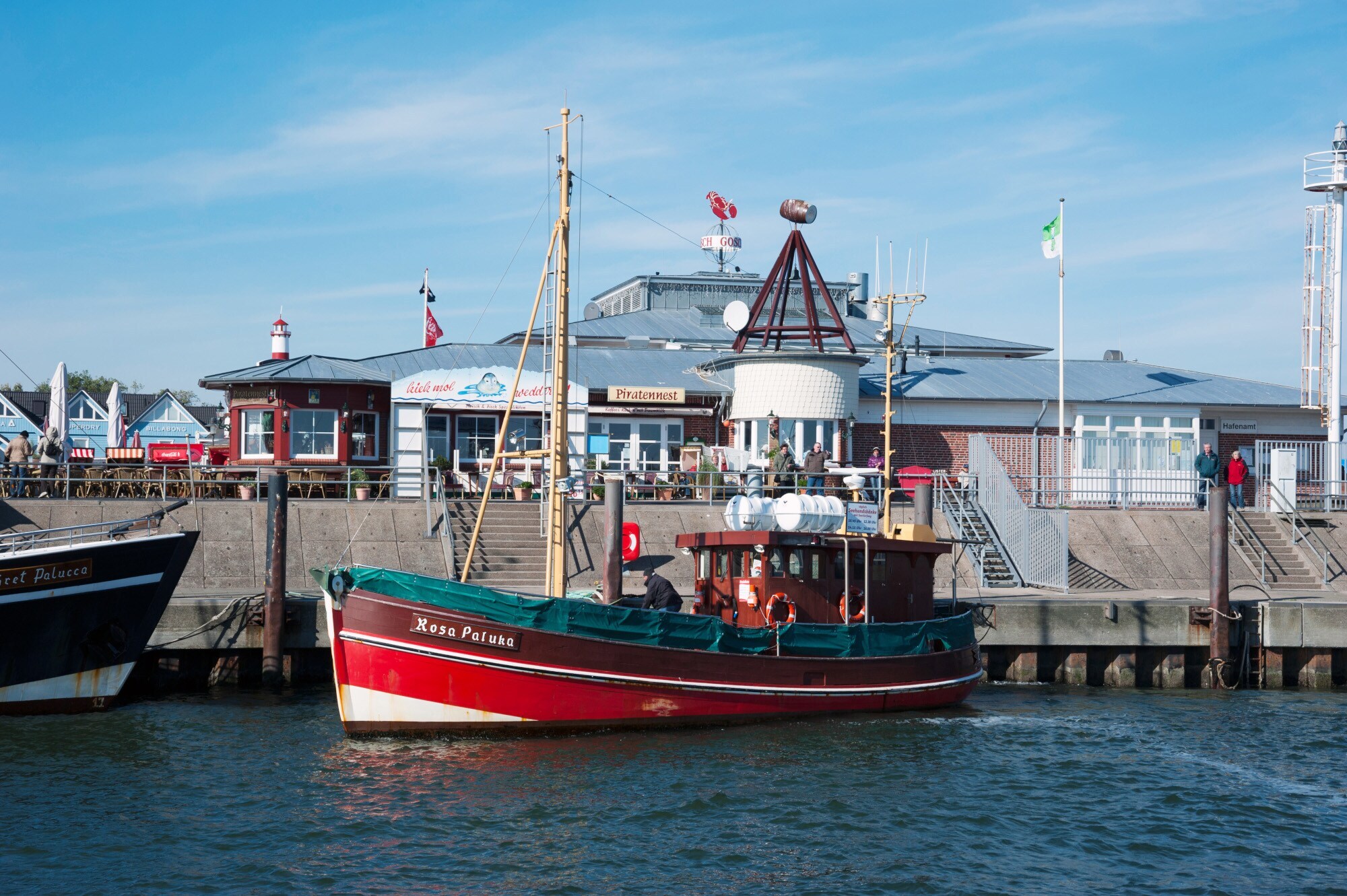 Ein Ausflugsboot an einer Hafenpromenade mit Geschäften
